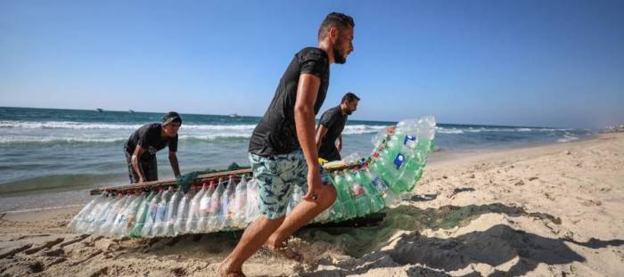 وسط استغراب الناس من حوله.. فلسطيني يُبحر على 700 عبوة بلاستيكية ليصطاد رزق عائلته، صور وفيديو